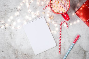 Kırmızı Noel süslemeleri, şekerli bir fincan kakao, alarm ve hediyeler içeren yılbaşı planları yazmak için günlükle birlikte düz bir kompozisyon. Yeni Yıl Planlaması. Defterdeki hedefler 