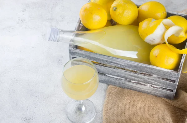 Cam şişede limoncello ve gri arka planda taze olgun sarı limonlar, geleneksel ev yapımı tatlı İtalyan limon likörü, güçlü alkollü içecek ve taze olgun limonlar..