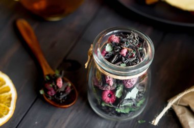 Nane aromalı sade çay ve kavanozda kuru ahududu ve koyu ahşap masada ahşap kaşık, meyve çerezi, bal ve pastille sıcak çay saati. Doğal ışık, seçici odaklanma