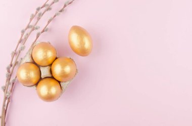 Söğüt dalları ve pastel pembe arka planda bir tepside altın rengi yumurta. Asgari paskalya konsepti. Mesaj için fotokopi alanı olan mutlu Paskalyalar. Üst görünüm, düz görünüm.