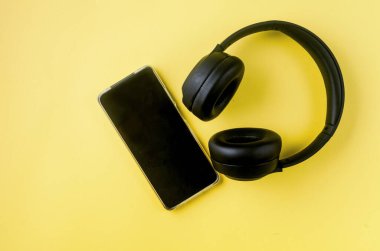 Sarı kağıtta kulaklıklı, boş ekranlı akıllı bir telefon. Konsept müzik dinlemek, döküm, akıllı telefondan ses.