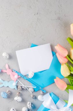 Boş Paskalya tebrik kartı ve mesaj yeri. Boş notlu zarf, paskalya yumurtaları, dekorasyonlar ve gri beton arka planda laleler. Tasarım için hazırlan. Tebrikler için şablon 