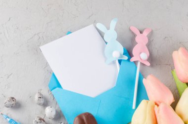 Boş Paskalya tebrik kartı ve mesaj yeri. Boş notlu zarf, paskalya yumurtaları, dekorasyonlar ve gri beton arka planda laleler. Tasarım için hazırlan. Tebrikler için şablon 