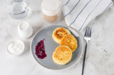 Krema, reçel ve bir fincan latte ile siyah tabakta süzme peynirli krep. Sağlıklı Kahvaltı. Ev yapımı yemek.