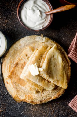 Ev yapımı krepler, koyu arkaplanda kahvaltı için gri tabakta tereyağlı lezzetli ince krepler. Geleneksel Rus mutfağı.