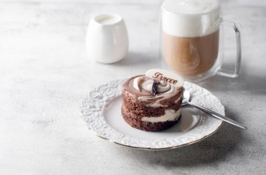 Zarif beyaz tabakta çikolatalı mini pasta ve açık gri arka planda cam bardakta köpüklü kapuçino. Lezzetli tatlı. Kahvaltı masası kurulumu. 