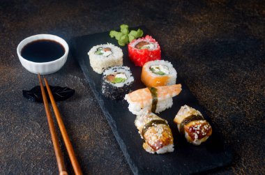 Siyah tabakta lezzetli suşi ruloları, soslar, yemek çubukları, zencefil ve wasabi. Suşi menüsü. Japon yemeği servisi. Çeşit çeşit suşi, dürüm, silah, nigiri. 
