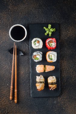 Siyah tabakta lezzetli suşi ruloları, soslar, yemek çubukları, zencefil ve wasabi. Suşi menüsü. Japon yemeği servisi. Çeşit çeşit suşi, dürüm, silah, nigiri. 