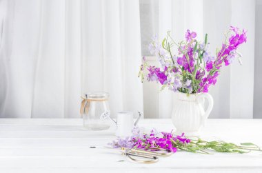 İç kısımda beyaz bir masanın üzerinde cam bir vazoda duran mor kır çiçekleri buketi. Kartpostallar boş. bahar konsepti