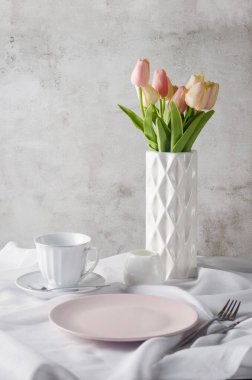 Sabah bahar sofrası dekorasyonu. Boş seramik tabak, bardak, temiz beyaz masa örtüsü arka planında vazoda taze laleler. Akşam yemeği veya kahvaltı konsepti, 