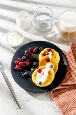 Donmuş yaban mersini, çilek, ahududu ve bir fincan latte ile siyah tabakta süzme peynirli krep. Sağlıklı Kahvaltı.