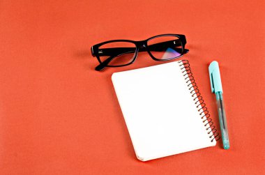 Boş beyaz defter, gözlük ve yeşil arka planda kalem. Metinler için minimalist konsept. Dekor ögeleri ile modelle
