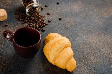 Taze kruvasan ve koyu beton arka planda bir fincan i sade kahve ve kahve çekirdeği. Sıcak içecekler, canlandırıcı bir kahvaltı..