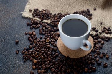 Koyu beton arka planda beyaz kahve ve kahve çekirdekleri. Sıcak içecekler, canlandırıcı bir kahvaltı..