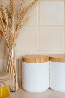 Tahta kapaklı mısır gevreği için kavanozlar, ahşap çatal bıçak takımı, kurutulmuş çiçekler ve mutfak masasındaki şişede sivri uçlar, İskandinav tarzı. Çevre dostu mutfak gereçleri ve dekorasyon, seçici odaklanma