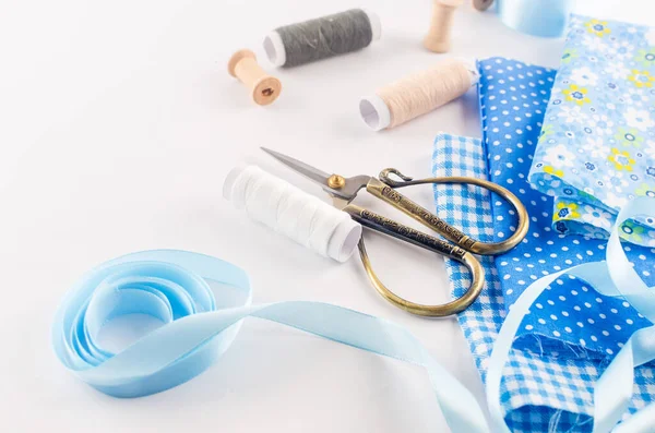 Set of blue sewing thread fabrics,  buttons and accessories on a white background. Flat lay composition with other sewing stuff.