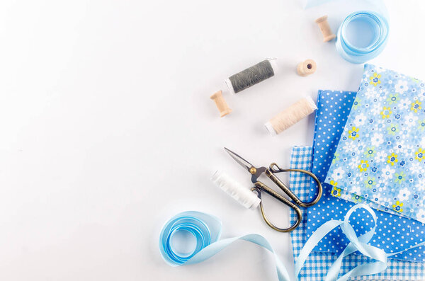 Набор тканей синей нитки, пуговиц и аксессуаров на белом фоне. Плоская композиция с другими швейными материалами.
