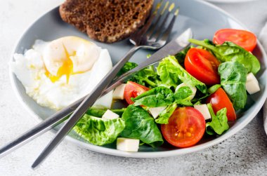Sabah bahar sofrası dekorasyonu. Tabakta salata, yumurta, bir fincan kahve ve kruvasan, temiz beyaz masa örtüsünde vazoda taze laleler. Kahvaltı masası beyaz renkte ayarlanıyor.