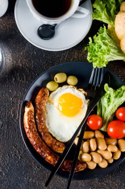 Geleneksel İngiliz kahvaltısı, kızarmış yumurta, sosis, fasulye, tabakta domates, kruvasan ve koyu arkaplanda kahve. Yukarıdan görüntüle 