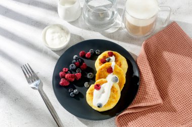 Donmuş yaban mersini, çilek, ahududu ve bir fincan latte ile siyah tabakta süzme peynirli krep. Sağlıklı Kahvaltı.