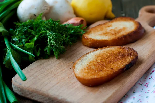 Fried slices of bread on a board, mushrooms, herbs and lemon. — Stock Photo, Image