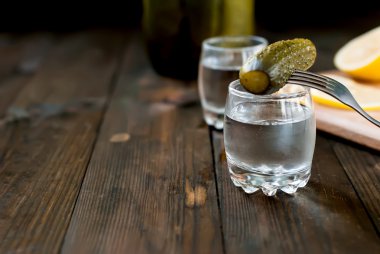 Cold vodka in a glass and cucumber on a wooden table clipart