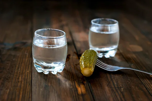 Cold vodka in a glass and cucumber on a wooden table — Stock Photo, Image