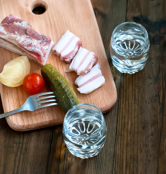 El vodka frío en el vaso y el pepino sobre la mesa de madera — Foto de Stock