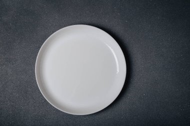 Koyu gri arka planda beyaz yuvarlak boş tabak, üst görünüm, kopyalama alanı. Yemek, yemek, diyet konseptini bekliyorum..