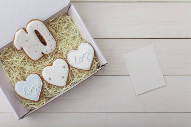 10 numara ve kalpler, beyaz ahşap masa arkaplanındaki mevcut kutuda zencefilli kurabiye şekillendiriyor. 10 numaralı konsept ve 14 Şubat Sevgililer Günü, modelle. Metin için yer.