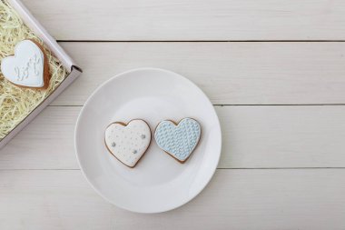 Hediye kutusu ve zencefilli kurabiye. Kalp şekilleri. Beyaz tabakta duran şekerler beyaz tahta masa zemininde duruyor. 14 Şubat Sevgililer Günü konsepti. Metin için yer.