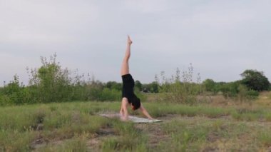 Spor kıyafetli çekici bir kadın gün batımında doğa arka planı üzerinde fiziksel egzersiz yapıyor. Yoga, esneme, sağlıklı yaşam tarzı. Yörünge atışı