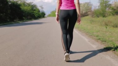 Spor giyimli genç bir kadın yeşil ağaçların arka planında dışarı koşmadan önce ya da sonra gidiyor. Yaklaş, sadece bacaklar ve kalçalar görünür. Spor, kilo verme konsepti.