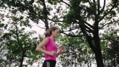 Spor giyimli genç bir kadın yeşil ağaçlar ve gökyüzü arka planında dışarı koşmaya başlıyor. Düşük açı. Spor, sağlıklı yaşam biçimi, spor, kilo verme konsepti.