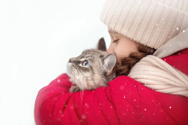 Kırmızı ceketli ve bej şapkalı bir kız bir kış günü bir kedi, bir köpek ve bir oyuncakla yürüyor..