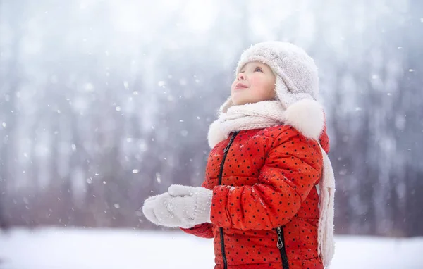 Turuncu ceketli ve yün şapkalı küçük bir kız kızak ve lolipopla karda yürüyor.
