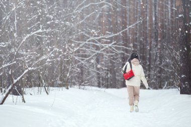 Beyaz ceketli ve kürklü bir kadın kış ormanında yürüyüşe çıkmış.