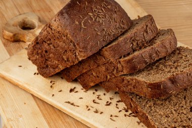 Dilimlenmiş çavdar ekmeği ve kimyon, tahtanın üzerinde yatıyor.