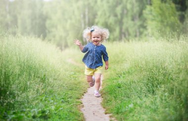 Kıvırcık sarı saçlı bir kız çayırda yürüyor, bir yaz günü.