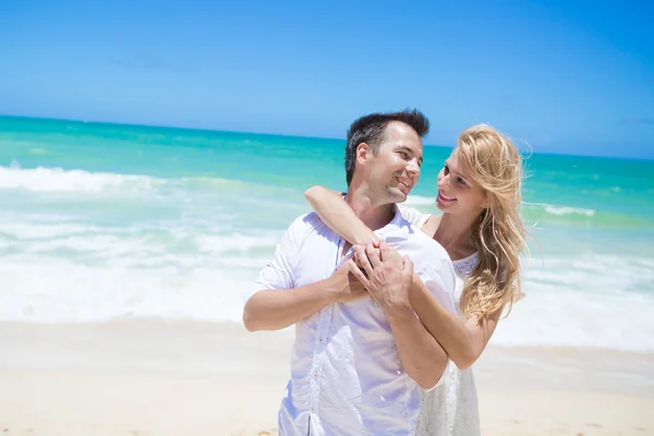 Χαρούμενο ζευγάρι αγκαλιάζει και να θέτουν στην παραλία μια ηλιόλουστη ημέρα — Φωτογραφία Αρχείου