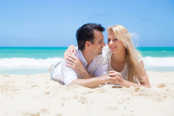 Cheerful couple embracing and lying on the beach on a sunny day — Stock Photo, Image