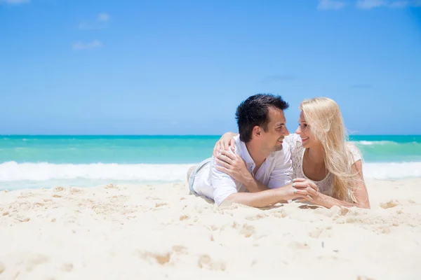 Cheerful couple embracing and lying on the beach on a sunny day — Stock Photo, Image