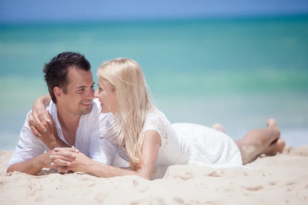 Cheerful couple embracing and lying on the beach on a sunny day — Stock Photo, Image