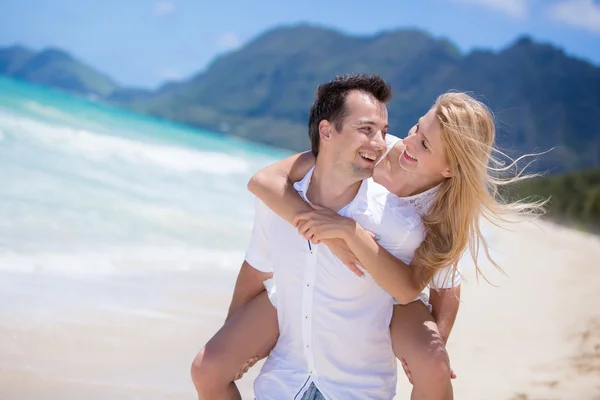Feliz jovem casal desfrutando de um solitário praia backriding — Fotografia de Stock