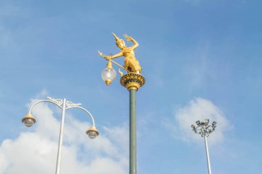 Sokak lambaları ve mavi gökyüzü arka planında spot ışıkları olan Tayland yerlilerinin altın heykeli.