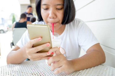 Akıllı telefon kullanan ve süt içen Asyalı kızın elini kapat.