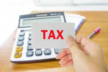 Hesap makinesinin, makbuzun ve kalem kaleminin arka plandaki bulanık fotoğrafı üzerinde kelime vergisi olan el bilgisayarı kartı