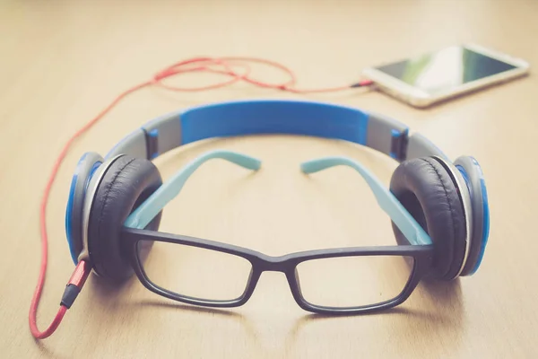 glasses headphone and smartphone on wood floor in retro filter : concept photo of listening to music from smart phone