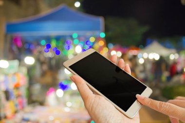 Geceleri açık hava pazarındaki insanların bulanık arka planında el yapımı akıllı telefon.