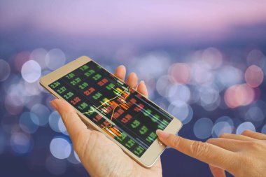 Elle kullanılacak akıllı telefon soyut bulanık bokeh backgrund üzerinde hisse senedi panosu üzerinde